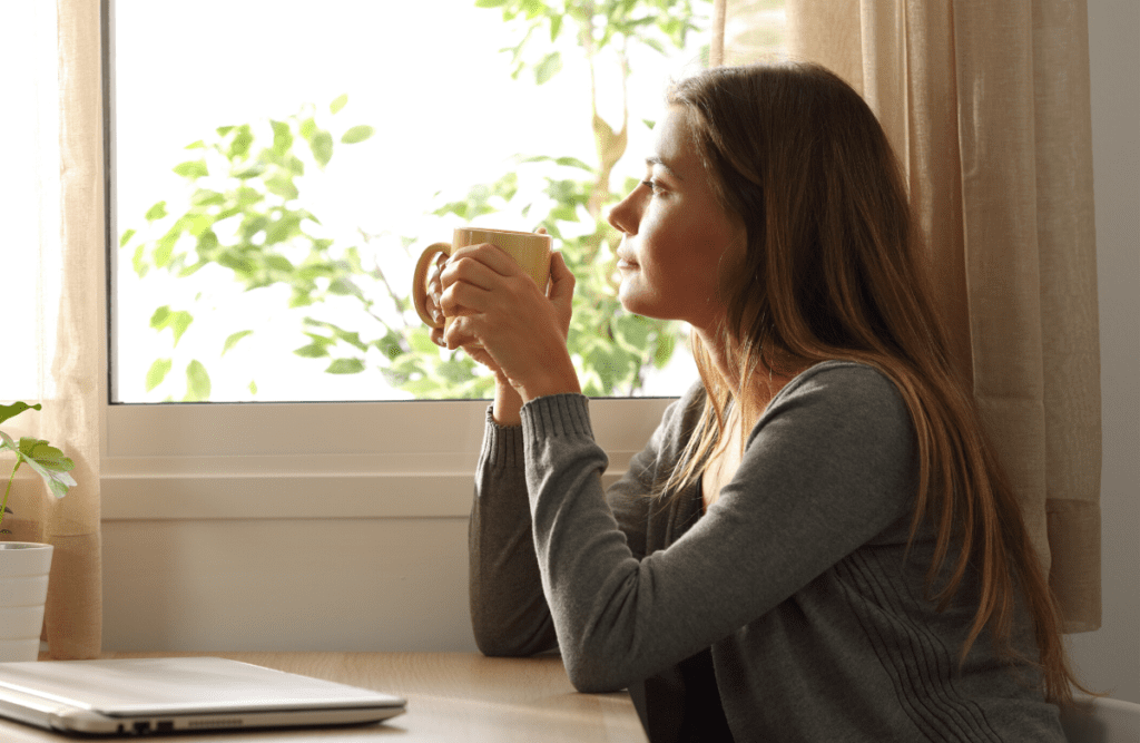 Woman sitting at the window while holding a mug.