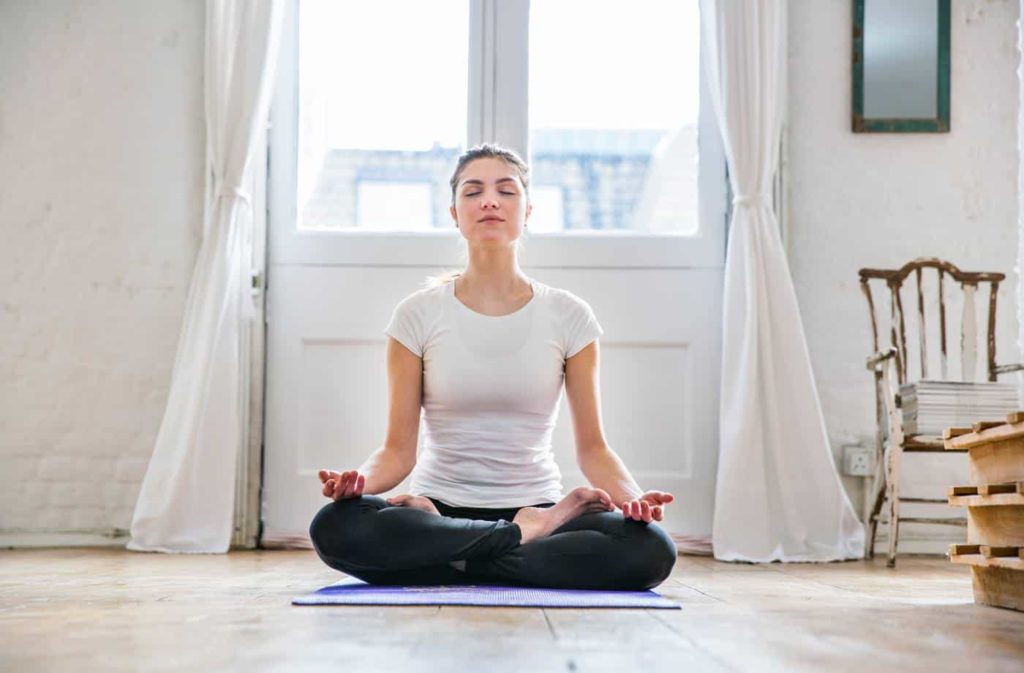 Woman sitting in front of window in lotus position.