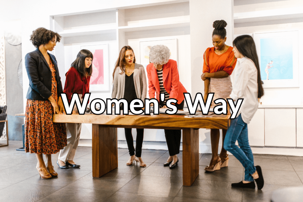 Businesswomen work around a wooden table behind text that says Women's Way.