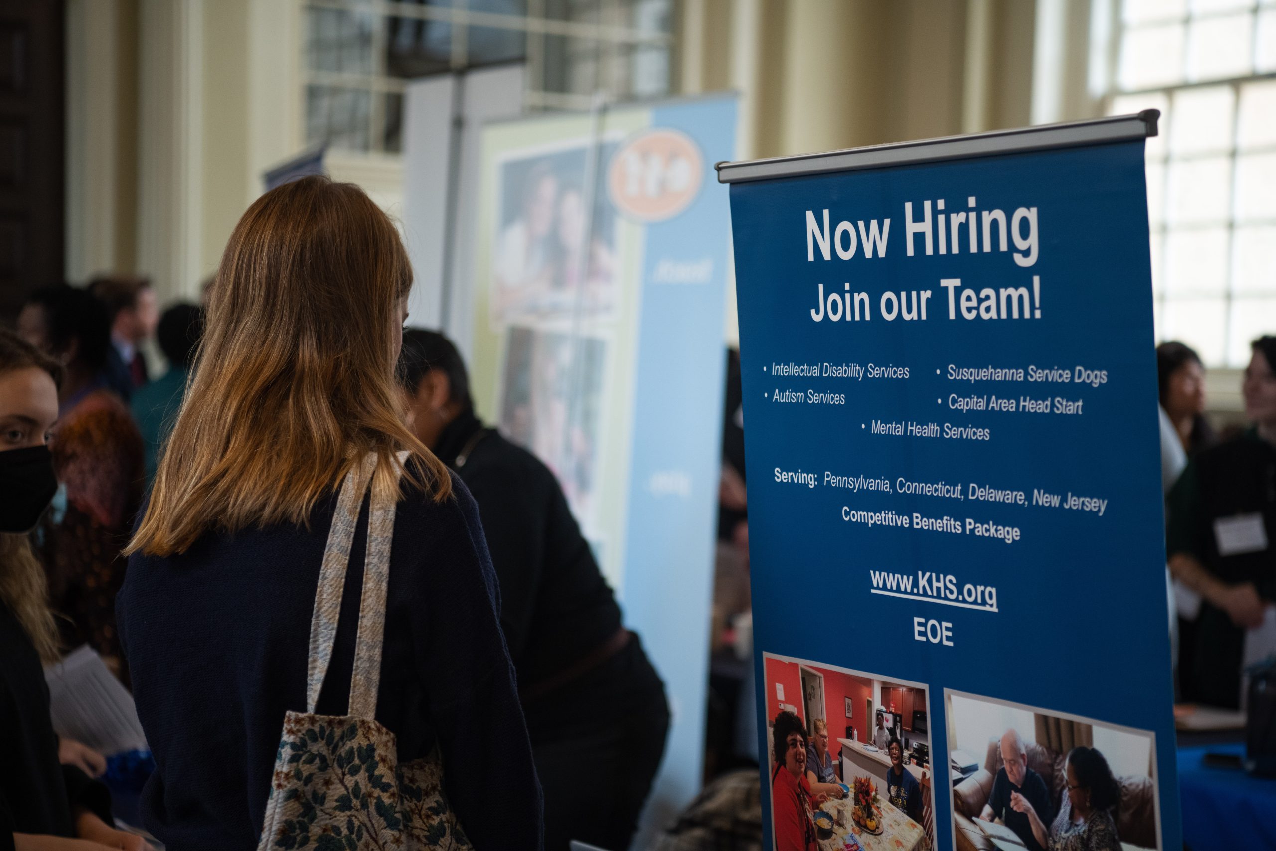A student at the Tri-College Career Fair next to a sign that says "Now Hiring." Photo taken by Holden Blanco '17.