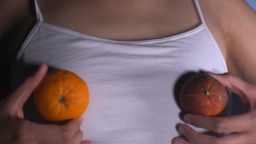 a person holds clementine oranges over their chest, one ripe, the other shriveled